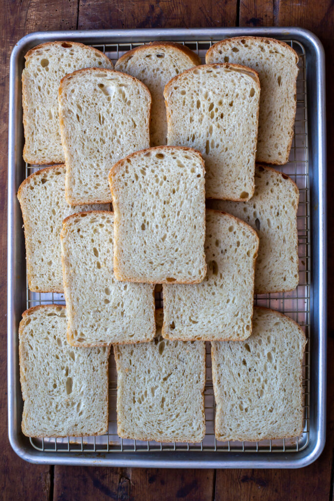 Overhead view of a sheet pan of slices of sourdough sandwich bread